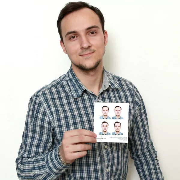 Молодой человек держит в руке фотографии на документы